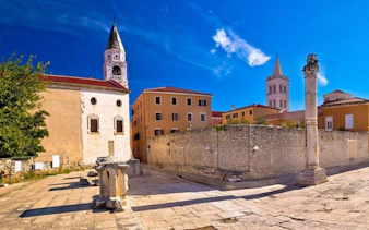 Historic Roman ruins and church towers in Zadar, Croatia, under a clear blue sky.