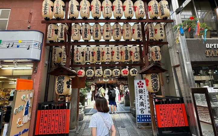 Kyoto Nishiki Market entrance with lanterns and visitors exploring shops.