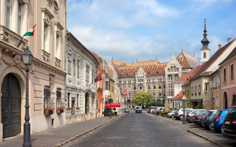 Street view in Buda Castle District, Budapest, with historic buildings and a distant church.