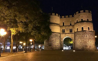Medieval gate illuminated at night in Cologne during haunted city exploration game.