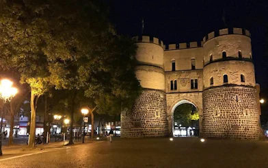 Medieval gate illuminated at night in Cologne during haunted city exploration game.
