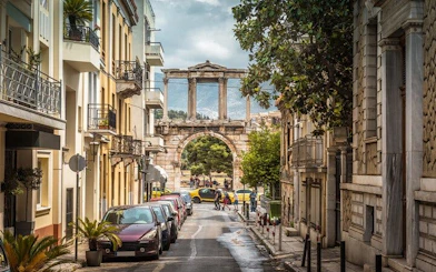 Street view of Hadrian's Arch in Athens, Greece, with parked cars and surrounding buildings.