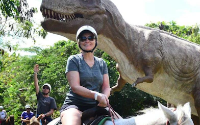Horseback riders near dinosaur statue in Punta Cana jungle setting.