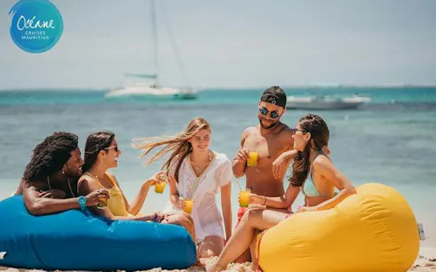 Group enjoying drinks on Île aux Cerfs beach with catamaran in background, Mauritius.