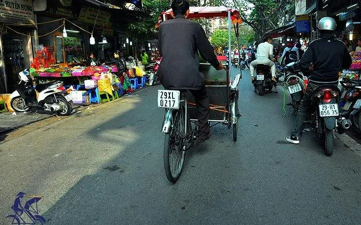 Cyclo navigating Hanoi Old Quarter street market with motorbikes and colorful stalls.