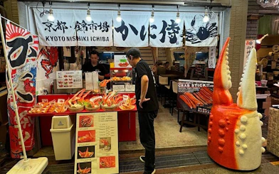 Kyoto Nishiki Market stall with seafood displays and giant crab claw decoration.