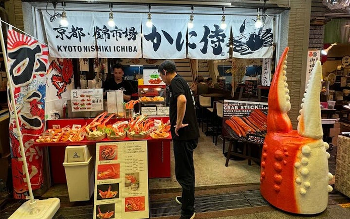 Kyoto Nishiki Market stall with seafood displays and giant crab claw decoration.