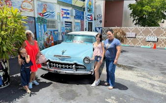 Visitors pose with a vintage car in Little Havana, Miami, surrounded by colorful murals.