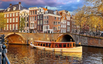 Amsterdam canal with boat and historic buildings during self-guided walking tour.