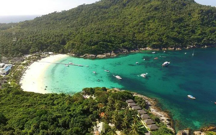 Aerial view of Banana Beach on Koh Hey with boats in turquoise water, surrounded by lush greenery, Phuket.