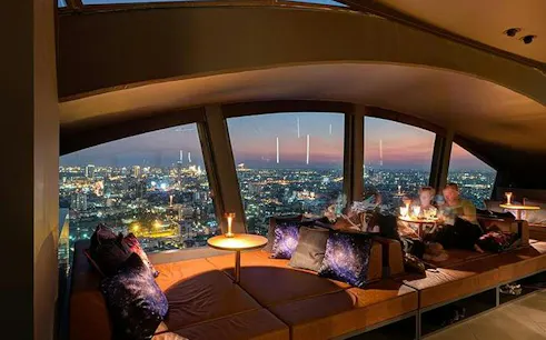 Skyline view from Vertigo TOO Sky Bar, Bangkok, with patrons dining at sunset.