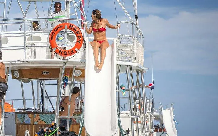 Catamaran with slide and guests enjoying Punta Cana cruise with drinks and snorkeling gear.