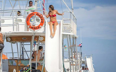 Catamaran with slide and guests enjoying Punta Cana cruise with drinks and snorkeling gear.