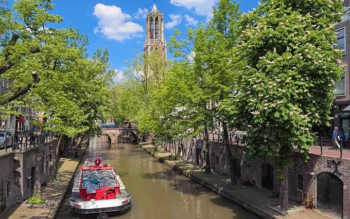 Utrecht canal with Dom Tower in background, featuring a tour boat under a clear sky.