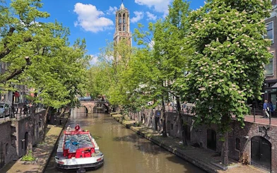 Utrecht canal with Dom Tower in background, featuring a tour boat under a clear sky.