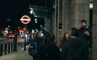 Group on Little Venice ghost walk near London Underground sign at night.