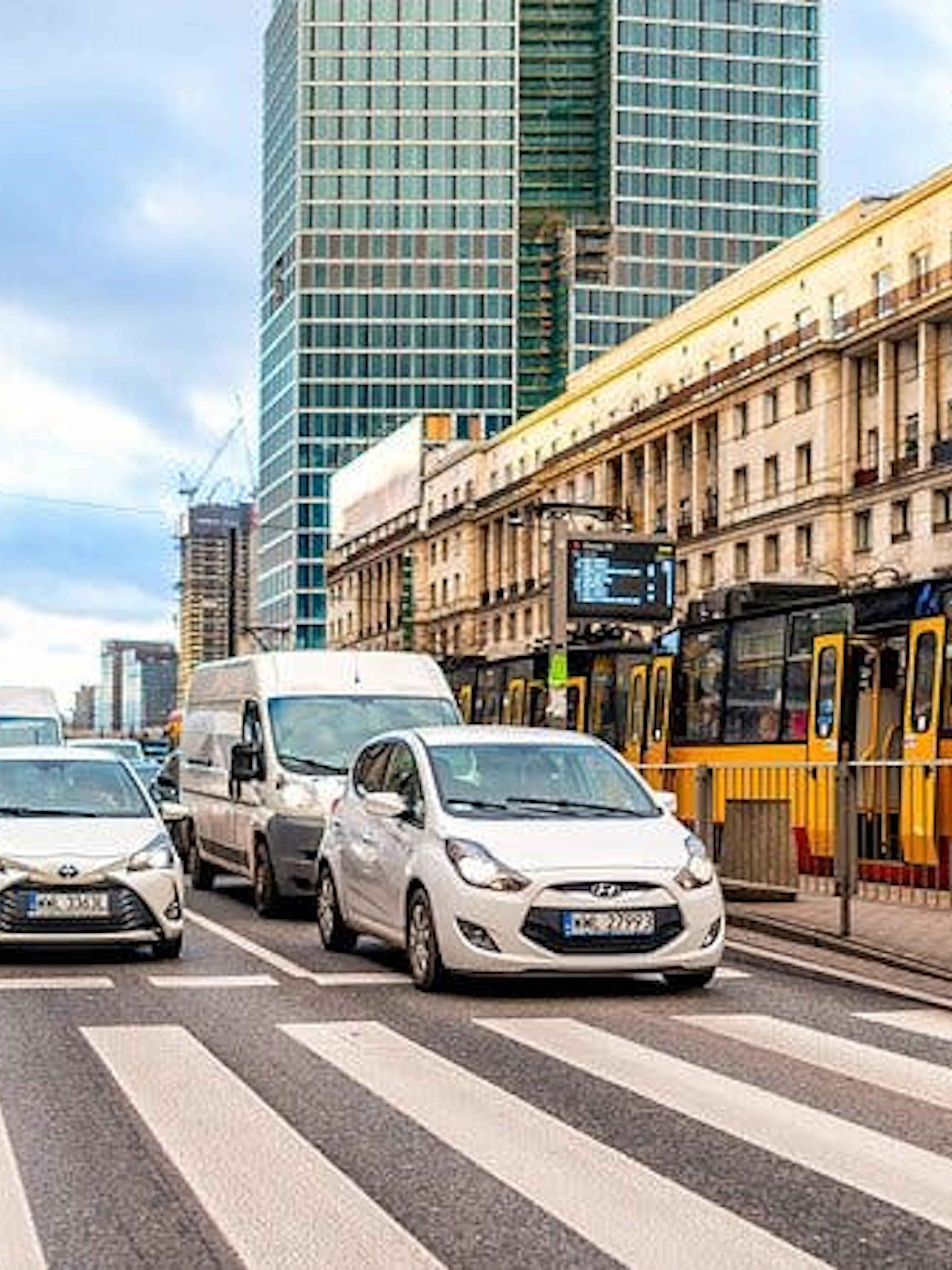 Warsaw street scene with cars, tram, and high-rise buildings in Muranów district.