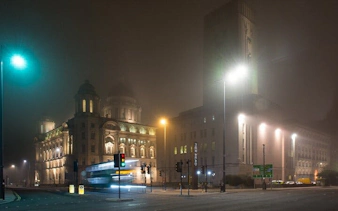 Liverpool cityscape at night with historic buildings and streetlights in fog.