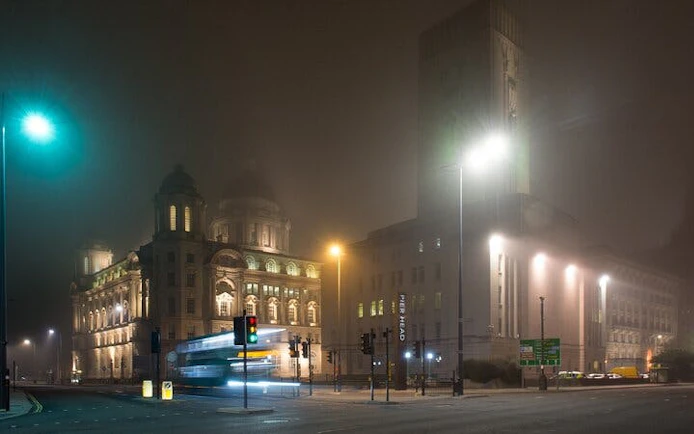 Liverpool cityscape at night with historic buildings and streetlights in fog.