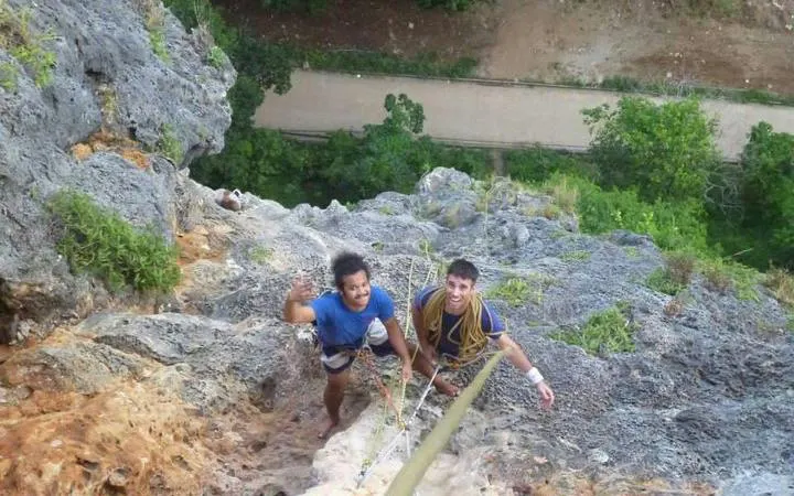 Rock climbers ascending limestone cliffs at Railay Beach, Krabi, with lush greenery below.