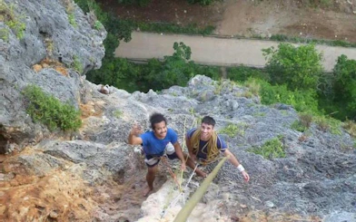 Rock climbers ascending limestone cliffs at Railay Beach, Krabi, with lush greenery below.