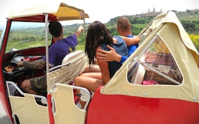 Tourists in a tuk tuk enjoying a scenic view of Tuscany's vineyards and hills.