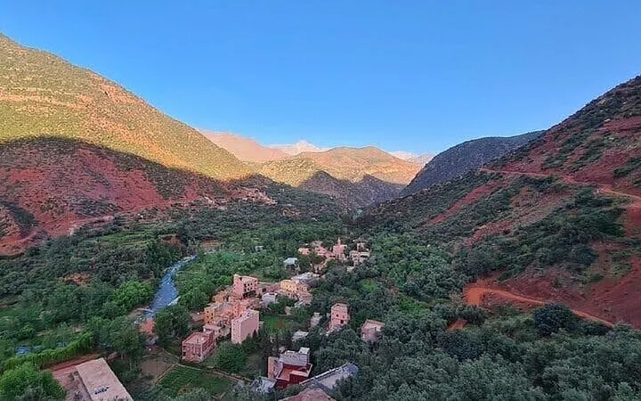 Berber village nestled in the Atlas Mountains near Marrakesh, surrounded by lush greenery and red hills.
