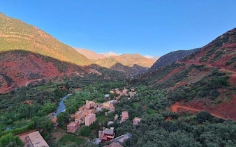 Berber village nestled in the Atlas Mountains near Marrakesh, surrounded by lush greenery and red hills.