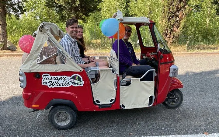 Tuk Tuk with tourists on Tuscany wine tour, featuring local guide and colorful balloons.