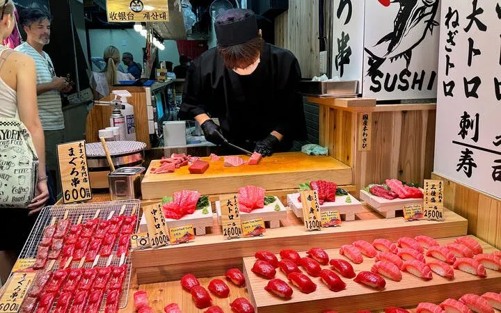 Sushi chef preparing fresh tuna at Nishiki Market, Kyoto, with various sushi selections displayed.