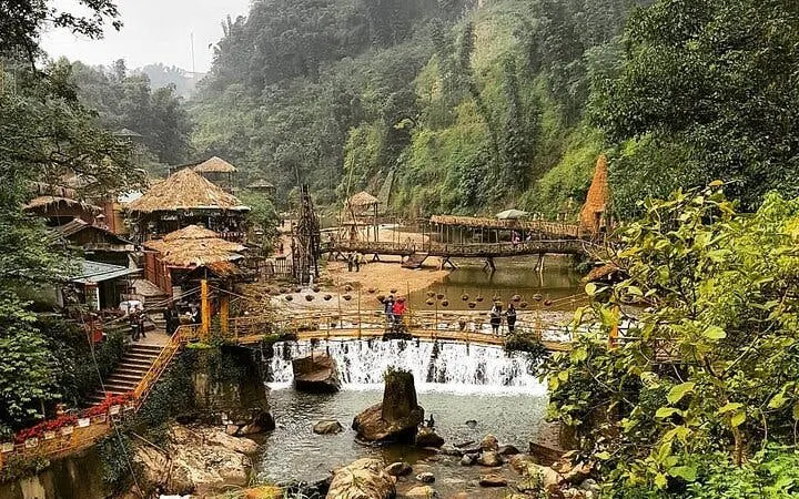 Visitors crossing a wooden bridge over a waterfall in Cat Cat Village, Sapa, surrounded by lush greenery.