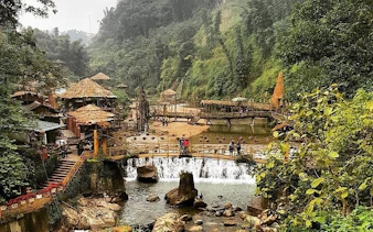 Visitors crossing a wooden bridge over a waterfall in Cat Cat Village, Sapa, surrounded by lush greenery.