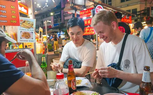 Street food tasting in Bangkok's Chinatown with diverse dishes and drinks.