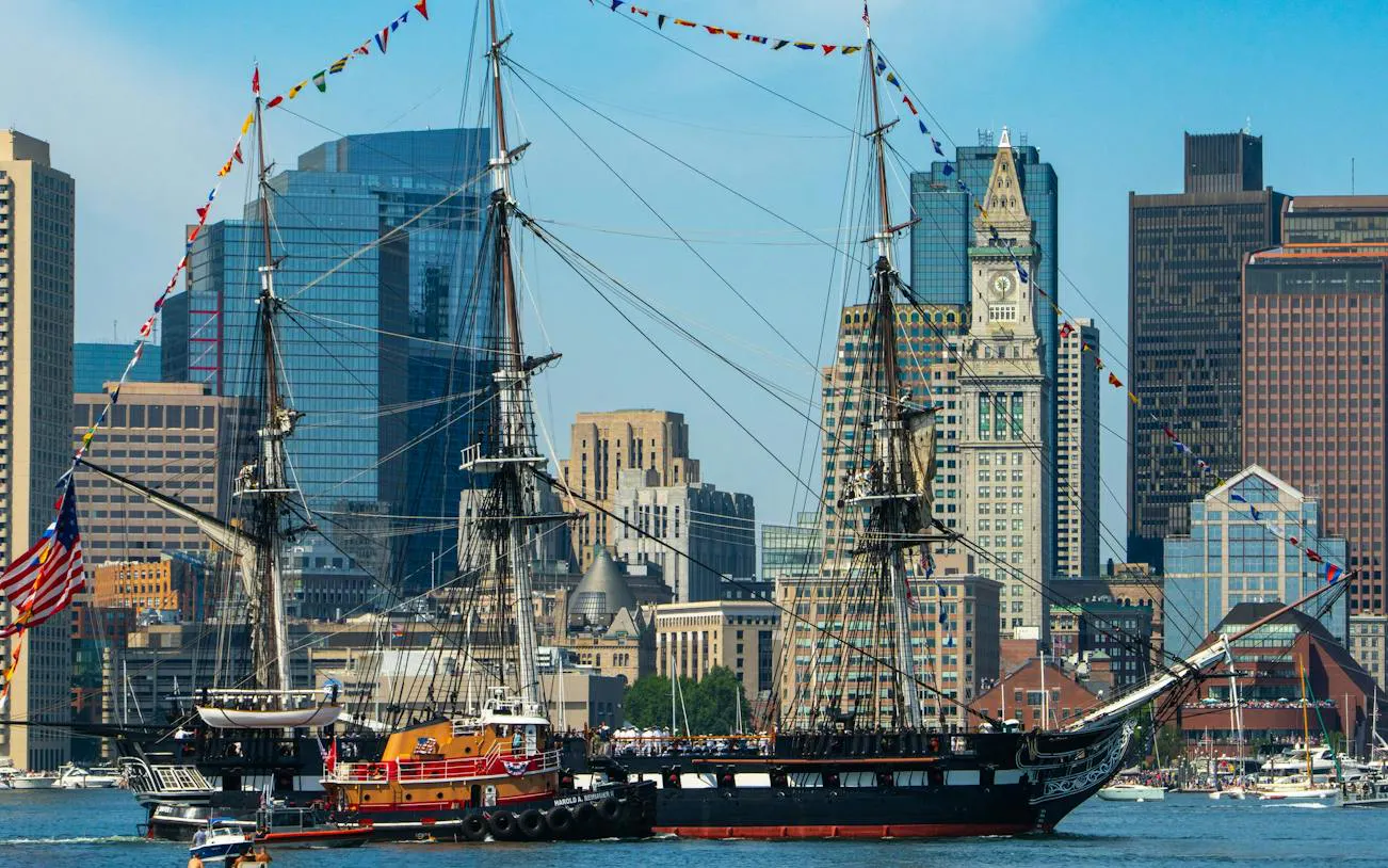 Historic ship USS Constitution in Boston Harbor with city skyline in the background.