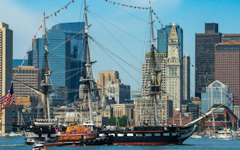 Historic ship USS Constitution in Boston Harbor with city skyline in the background.