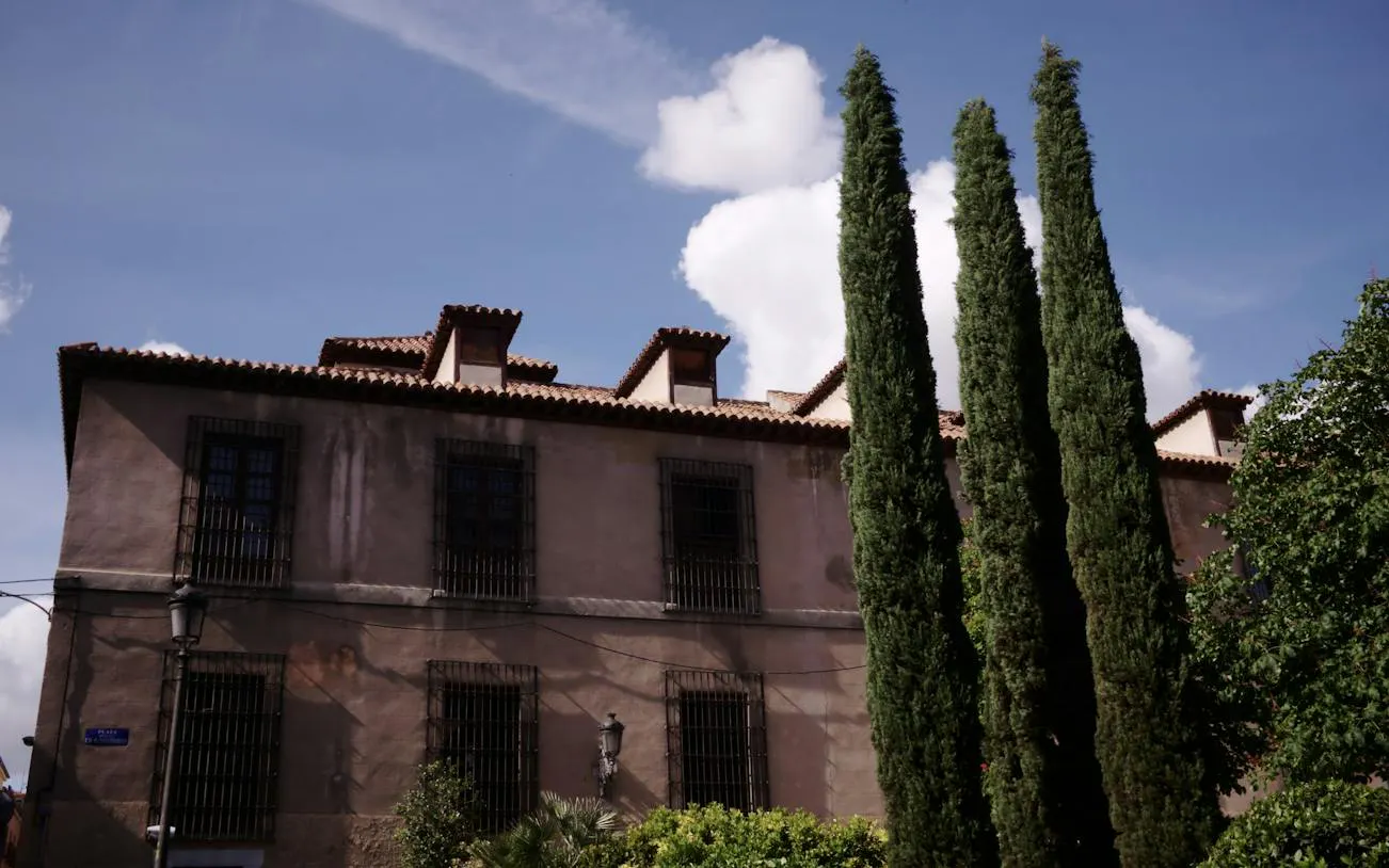 Historic building with tall cypress trees in Malasaña, Madrid.