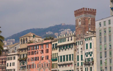 Historic buildings along a street in Genoa with hills in the background.