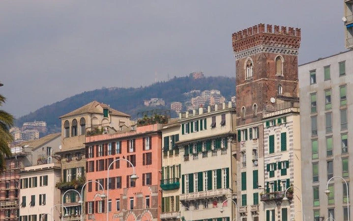 Historic buildings along a street in Genoa with hills in the background.
