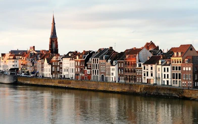 Riverside view of Maastricht's historic buildings and church tower during a self-guided walking tour.