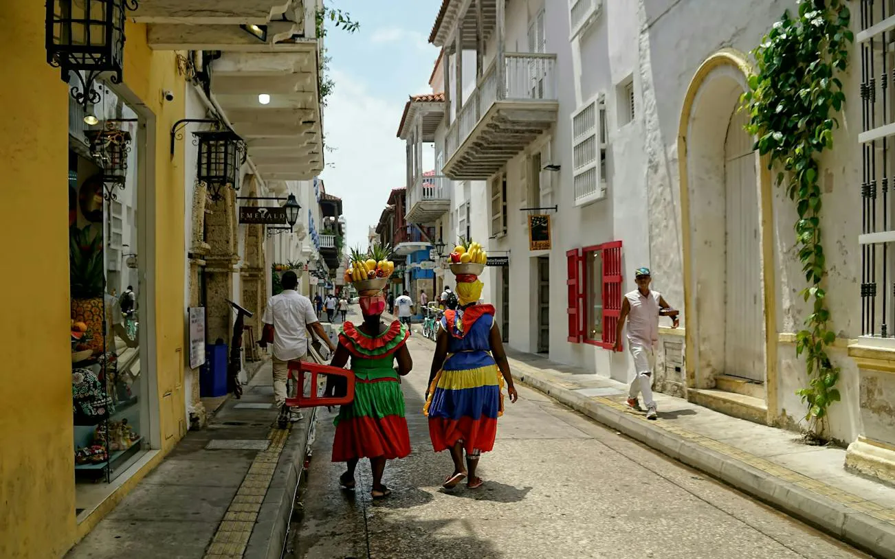 Street scene in Cartagena Walled City with women in traditional dress carrying fruit baskets.