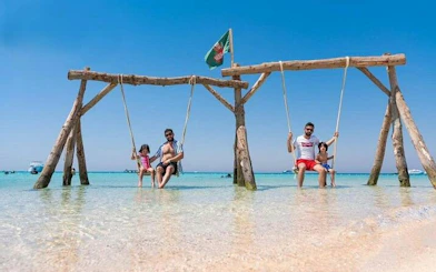 Private speedboat trip guests on swings in clear waters of Hula Hula Island, Hurghada.