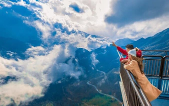 Couple on Sapa motorbike tour viewing mountains and clouds from a scenic overlook.