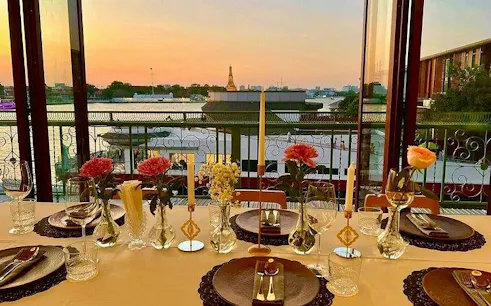 Fine dining setup overlooking Chao Phraya River at sunset, Bangkok.
