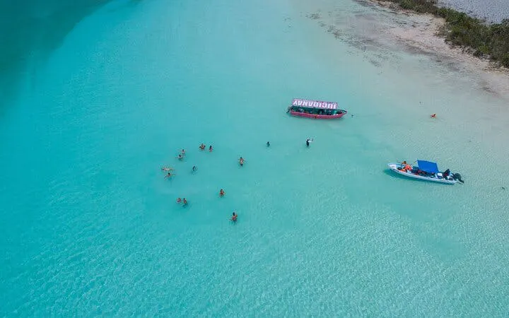 Visitors swimming in Bacalar Lagoon near pontoon boats during a day trip from Cancun.