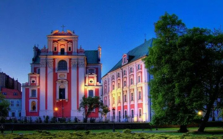 Poznan Fara Church illuminated at dusk, featured in self-guided audio tour via mobile app.