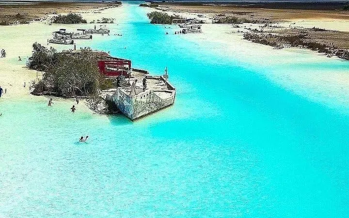 Bacalar Lagoon with pontoon boat and swimmers, part of Cancun day trip with cenote visits.