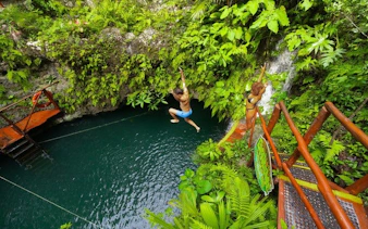 Person jumping into a cenote surrounded by lush greenery on a snorkeling tour in America’s largest reef.