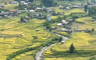 Rice terraces and village in Sapa, Vietnam, with a stream running through the landscape.