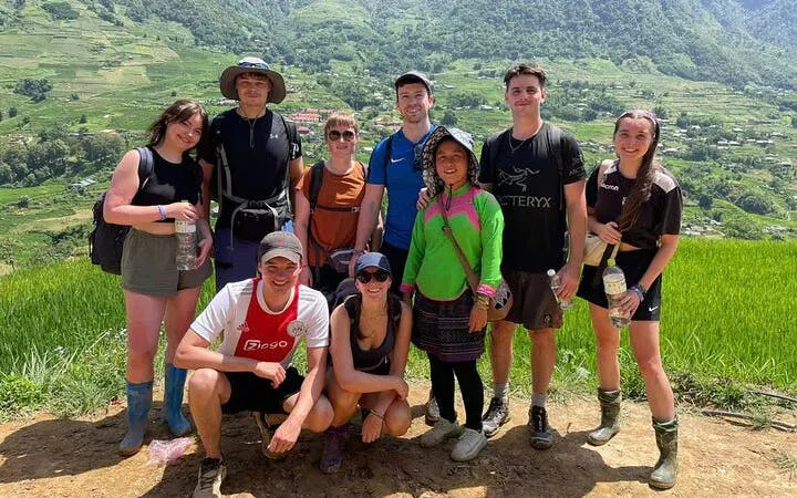 Group of trekkers with local guide on Sapa's Y Linh Ho trail, rice terraces in background.