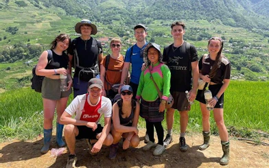 Group of trekkers with local guide on Sapa's Y Linh Ho trail, rice terraces in background.